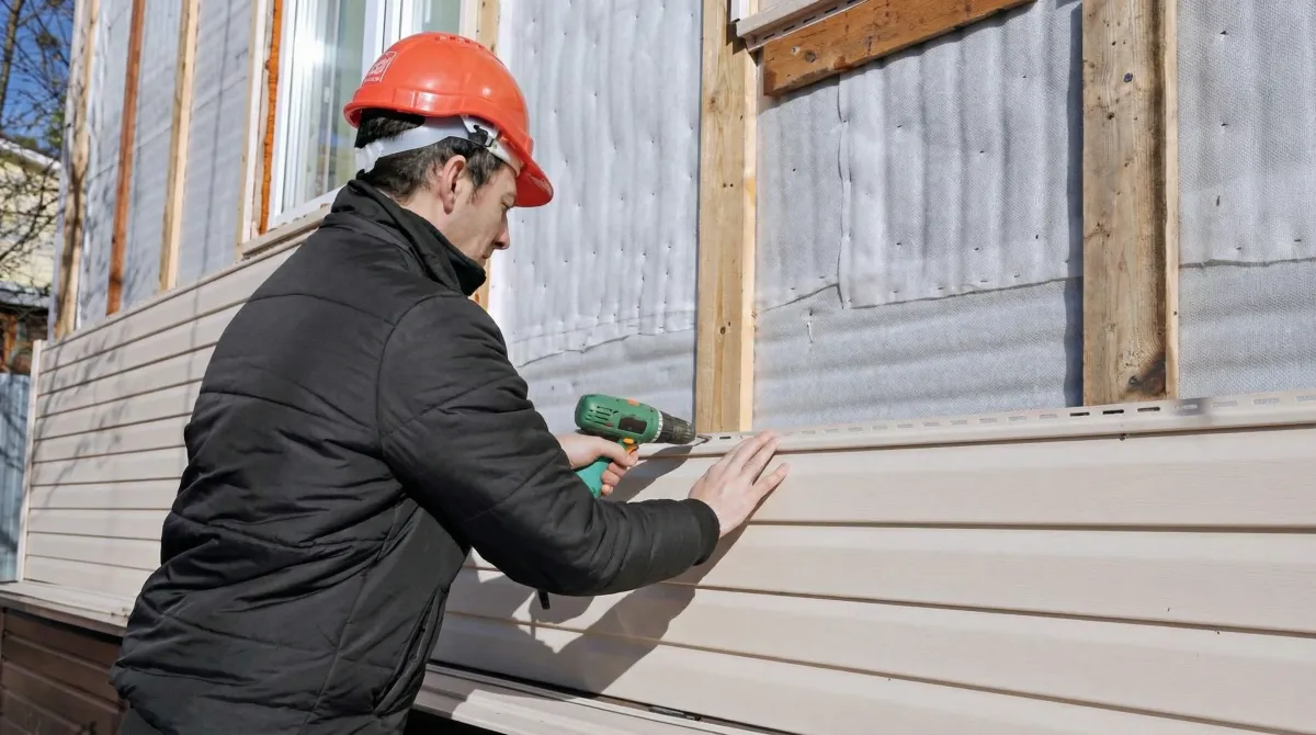 Siding replacement professional using a power drill to install new tan vinyl siding on a home exterior in Cape Coral, FL